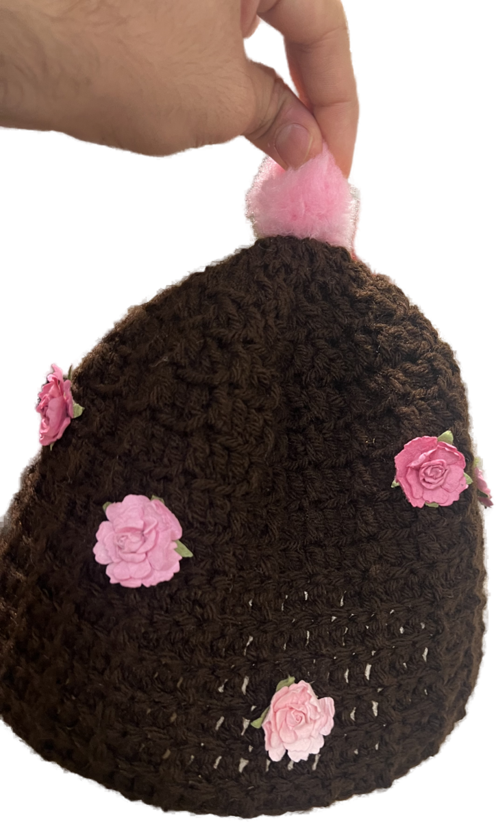 a hand pinching a pink pom pom at the top of a crocheted beanie
